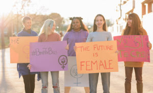 five ethnically diverse femme women holding signs including one that says the future is female